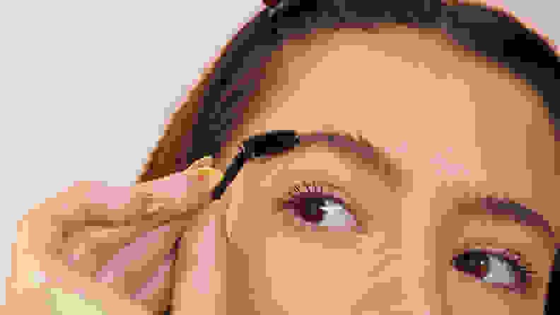 A closeup on the top half of a model's face as they hold a spoolie up to their eyebrow.