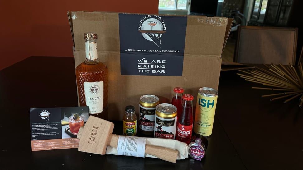 Everything that comes with a package of Raising the Bar, including bottled and canned drinks, alongside a wooden mallet with a cloth bag. Included is also a greeting pamphlet from the company.