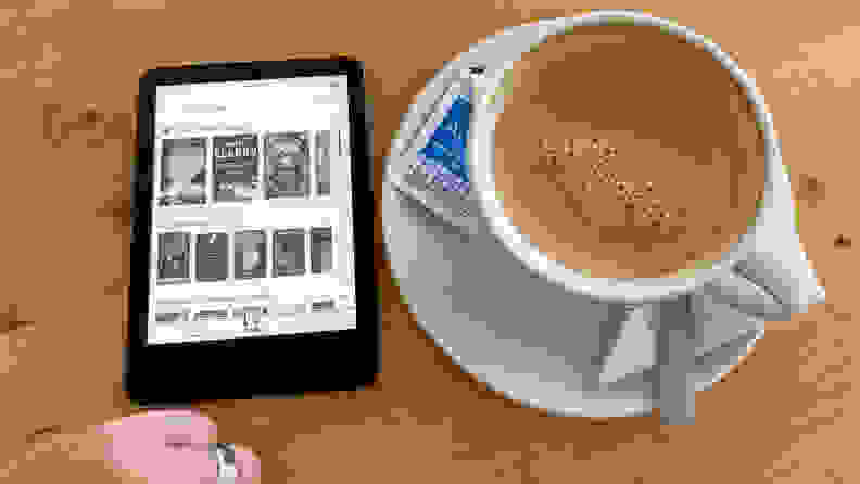 An Amazon Kindle e-reader sits on a table next to a large cup of coffee