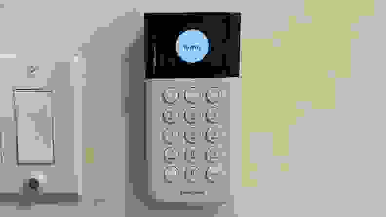 A SimpliSafe keypad hangs on a white wall.