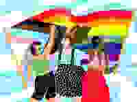 Graphic of three people wearing colorful outfits with the pride flag and trans visibility flag behind them