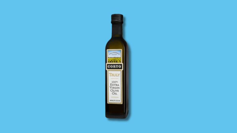 Slim, black rectangular bottle of Corta Extra Virgin Olive Oil in front of blue background.
