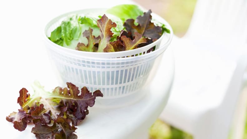 Eine mit frischem Salat gefüllte Salatschleuder auf einer weißen Arbeitsplatte.