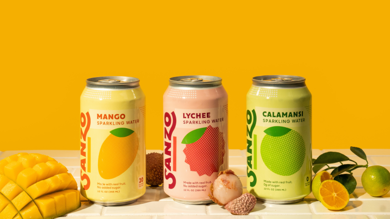 Against a orange backdrop, there are three cans of Sanzo sparkling water flavored with real fruits from Asia.