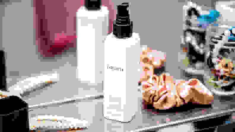 A white square-shaped bottle of hair detangler next to hair accessories