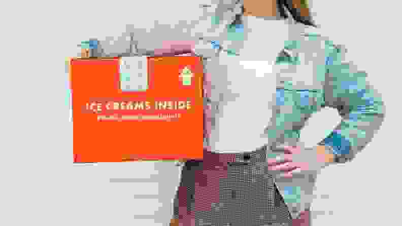 A person holds a bright orange cardboard box with the Jeni's Splendid Ice Creams logo on it.