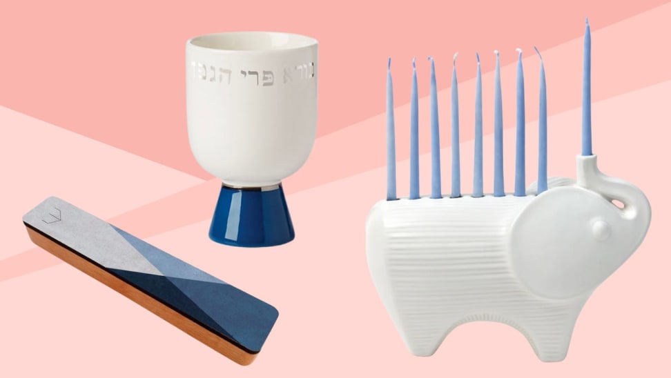 Blue and white mezuzah, kiddush cup, and an elephant shaped menorah in front of pink background.