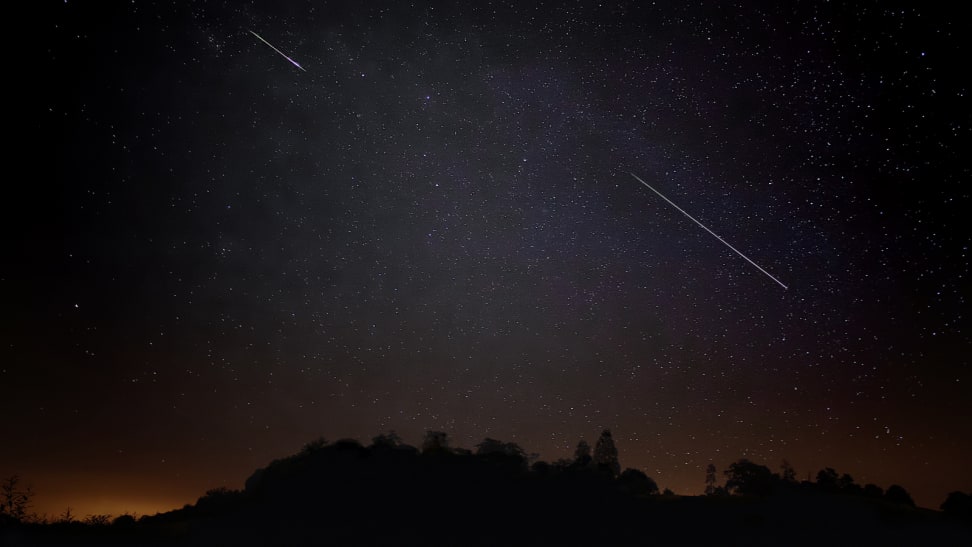 Night sky with meteors streaking, silhouette of forest below