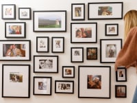 A woman adjusts a photo on a Framebridge gallery wall
