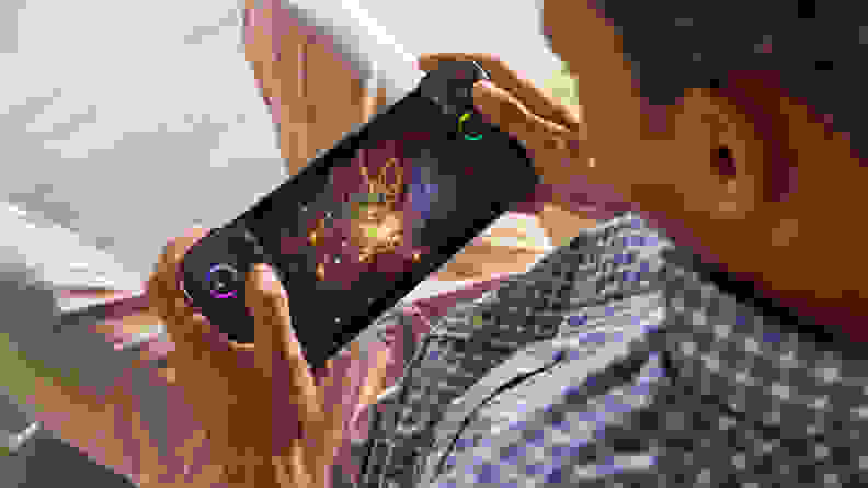 Someone playing a game on the Asus ROG Ally X while sitting on a couch, shot over their shoulder down at the handheld console.