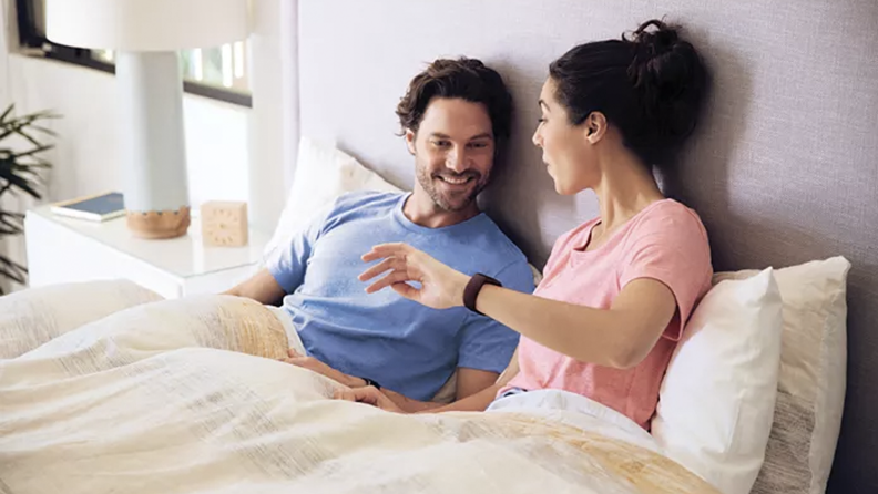A couple in bed looking at a Fitbit