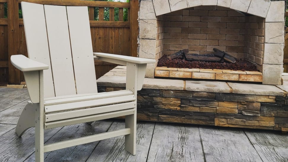 A picture of the Polywood Modern Curveback Adirondack chair in front of a fireplace.
