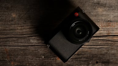 A black Leica Q (Typ 116) camera sits on a wooden table facing up