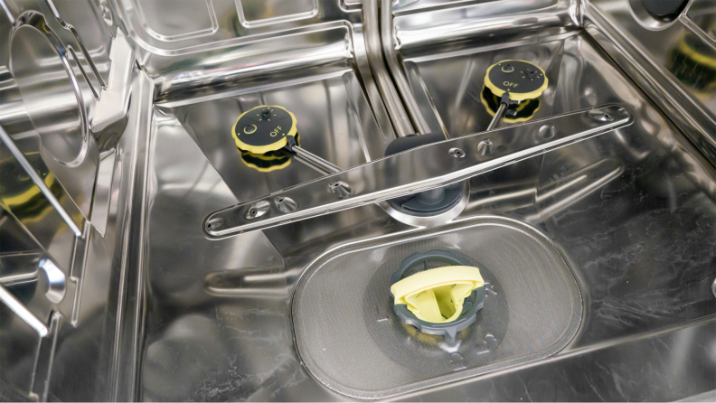 Two adjustable spray nozzles, a mesh-covered drain, and a spray arm are visible inside the stainless steel interior of the dishwasher.