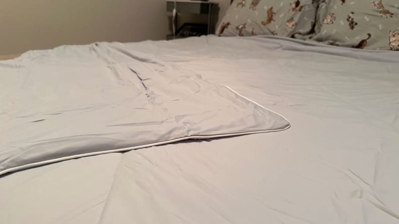Close-up view of a gray Cozy Bliss comforter spread out on a bed with one corner folded over, in front of a beige wall.