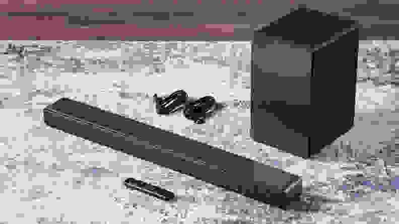Black, rectangular TCL Q Series (Q6310) 3.1-Channel Soundbar sitting on top of carpet next to two power cords