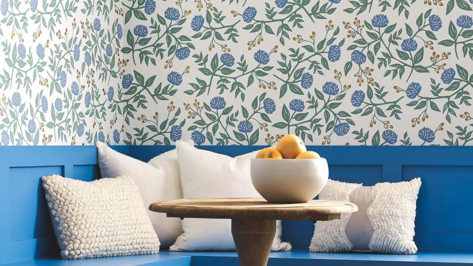 Blue wooden seating in the corner with white pillows and a blue floral decorative wallpaper from Rifle Paper Co.
