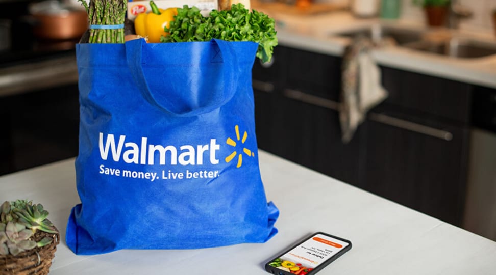 A bag of groceries sits inside of a blue Walmart bag next to a smartphone on a kitchen countertop