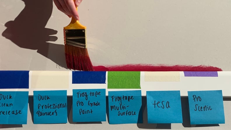 Person painting over crown molding on a drywall sheet with 3-inch painter's tape strips, all labeled with sticky notes.