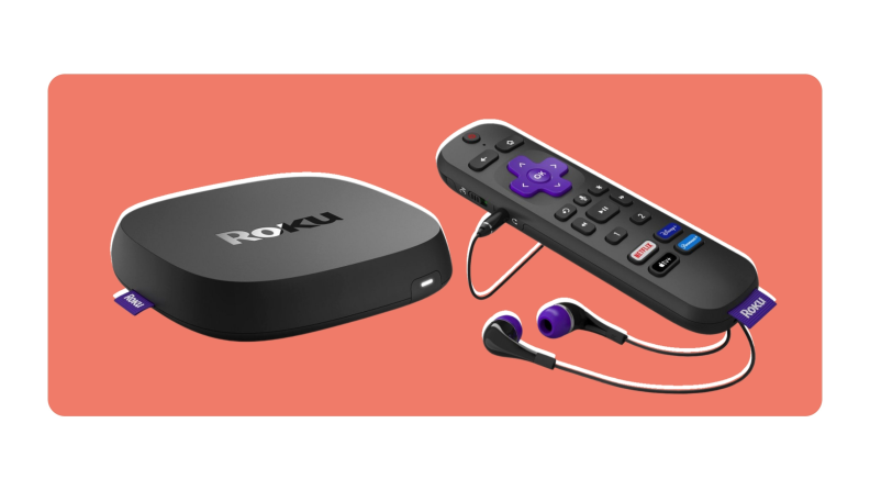 A Roku streaming device next to a Roku remote with a pair of wired headphones plugged into the side.