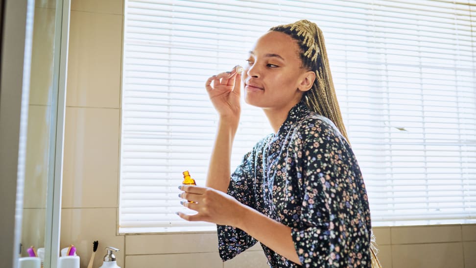 A person looking into a mirror and applying skincare to their face.