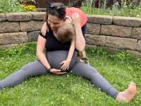 A pregnant woman sitting on the grass holding her bump and hugging an older child