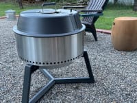 A portable charcoal grill sits on a pebble-covered yard.