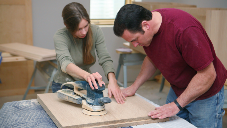 Man and woman sanding wooden surface together