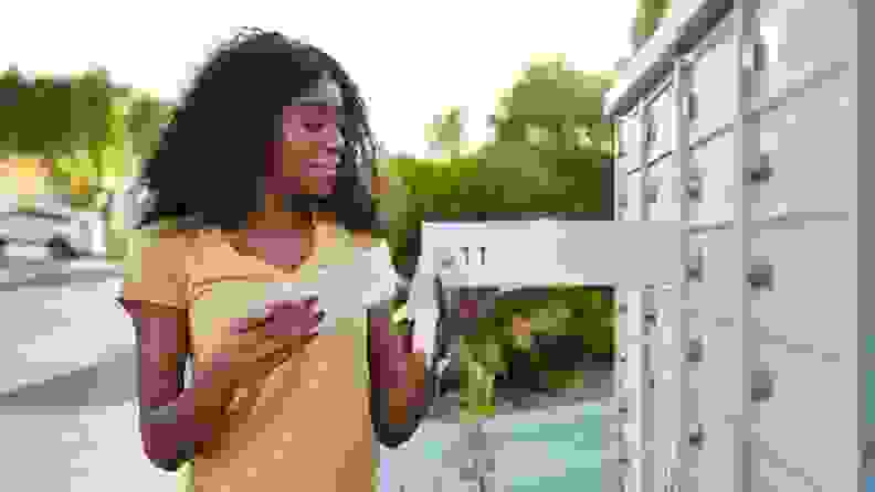 A woman standing next to open mailbox holding envelopes