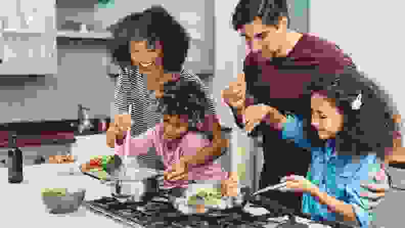 Two parents cook with the help of two children.