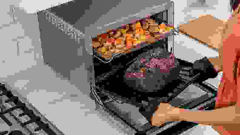 Person pulling pork roast out of Ninja oven, with roasted potatoes on the top shelf