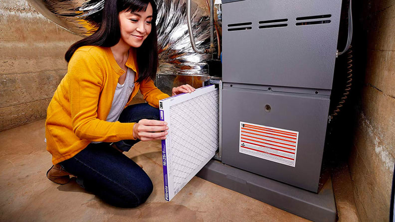 A woman kneels beside a furnace, changing in a new Filtrete Micro Allergen Defense Air Filter.