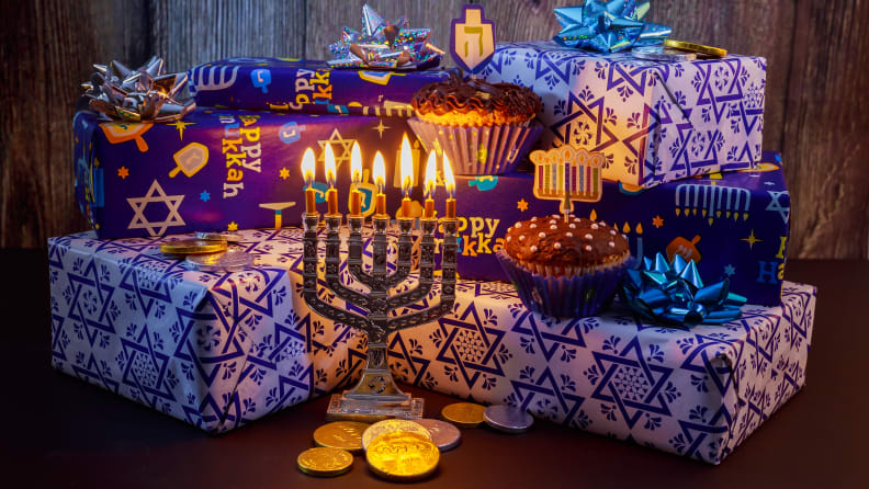 A pile of wrapped Hanukkah packages with a lit menorah in front.