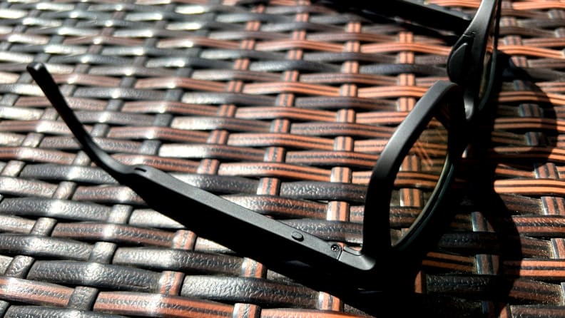 The Dusk sunglasses sit upside down on a brown and black background with a button in view.