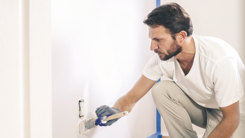 A person paints around a wall outlet.