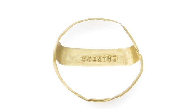 A white and gold jewelry dish that says "breathe."