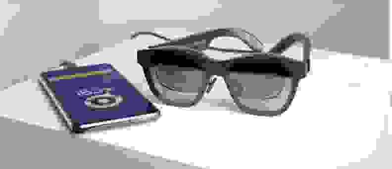 a pair of ar glasses next to a smartphone with the xrai glass app