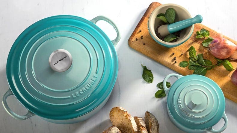 A teal Le Creuset dutch oven sitting on a countertop next to a charcuterie board.