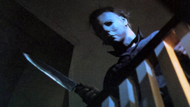 Michael Myers with a butcher knife leering over a staircase railing.