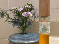 Living Libations Seabuckthorn Oil sits on a bathroom vanity in front of a floral arrangement.