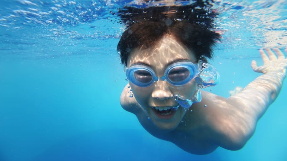 Asian boy swimming underwater. Shallow DOF with focus on foreground bubbles.