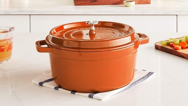 A bright orange Staub Dutch oven sits on a white kitchen counter.