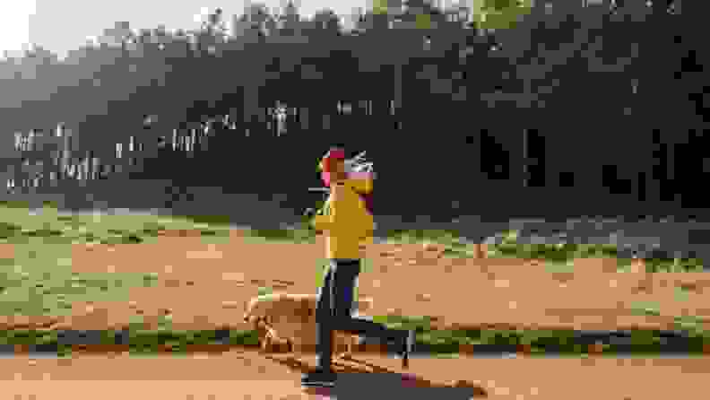 A runner in a yellow jacket jogs with their dog on a rural trail
