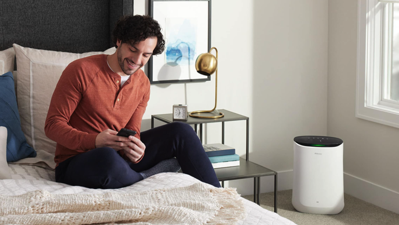 Person sitting on top of bed in bedroom while smiling at smartphone.