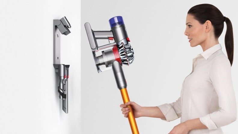 An image of a woman hanging her cordless vacuum from a wall hanger.