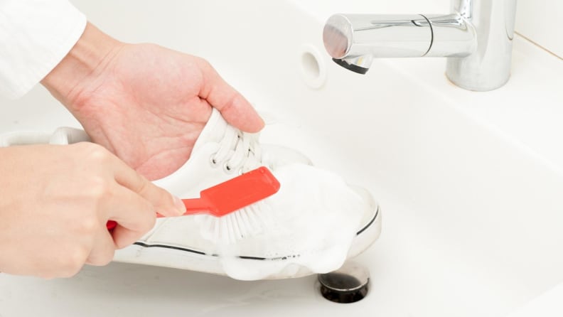 Person washing shoes with soap and brush in the sink.