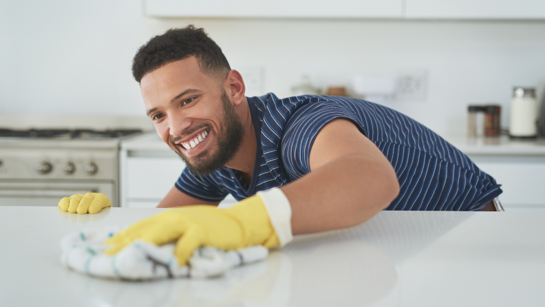 A man wearing yellow rubber gloves wipes down a counter with a rag.