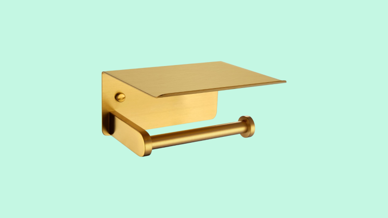 The Toilet Paper Holder with Phone Shelf Brushed Gold in front of a background.