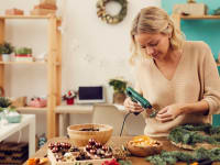 Woman using a hot glue gun to attach dried fruit to an evergreen Christmas wreath