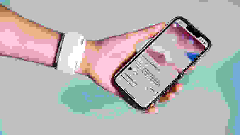 A person holds a cell phone while wearing a white stress tracker on their wrist.